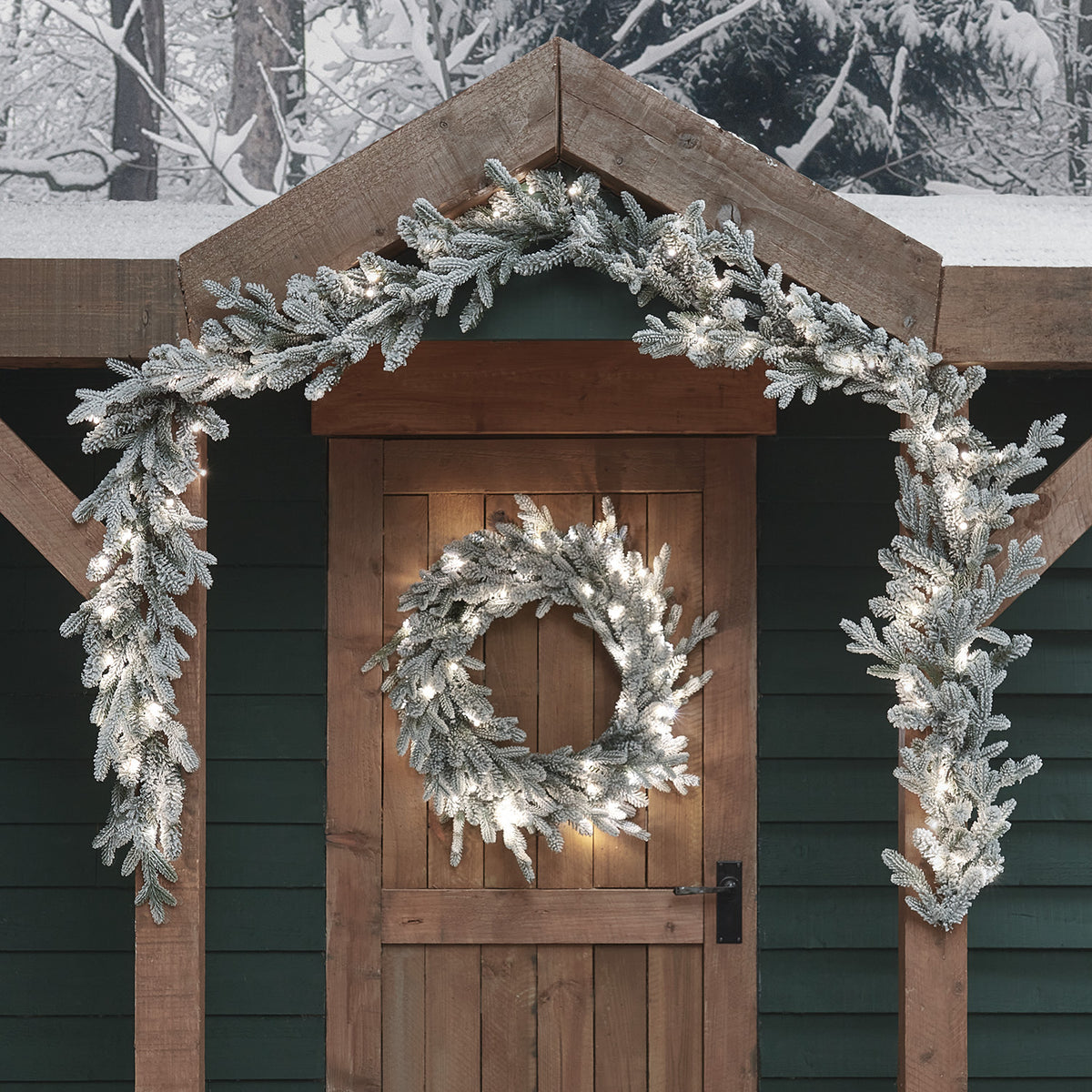 Weihnachtsgirlande und Kranz mit weißen LEDs beleuchtet an Holztür und Dachgiebel