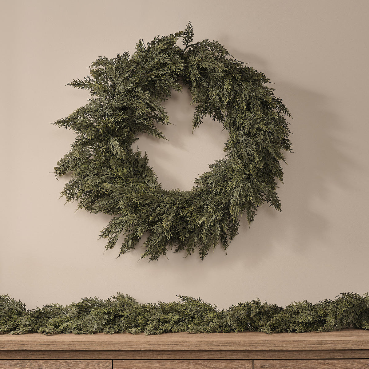 Unbeleuchteter Weihnachtskranz aus künstlichem Nadelgrün an Wand über Holzkommode