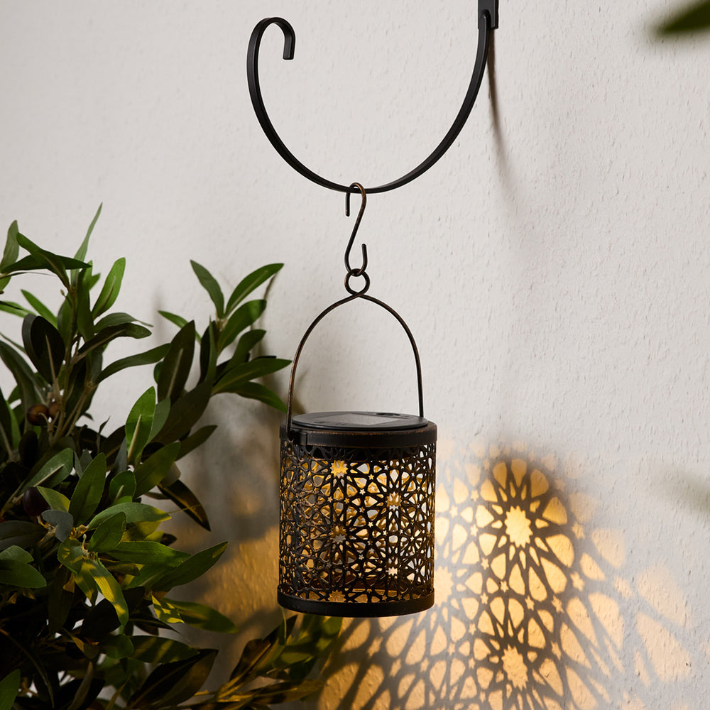 Marokkanische Solar-Hängelaterne mit Muster, leuchtet warmweiß an Wand, hängt an schwarzem Metallhaken