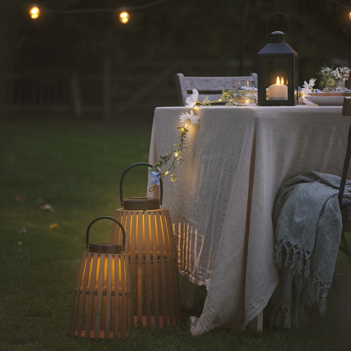 Große und kleine Bambus-Solarlaterne mit warmweißem Licht neben gedecktem Gartentisch