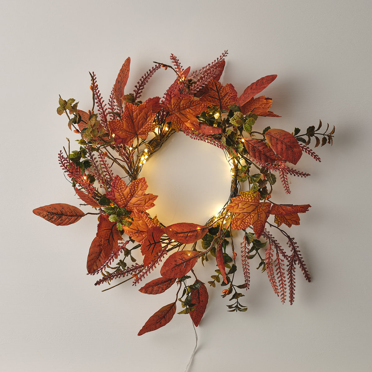 Herbstkranz mit orangefarbenen Ahornblättern und Micro LED Lichterkette an weißer Wand