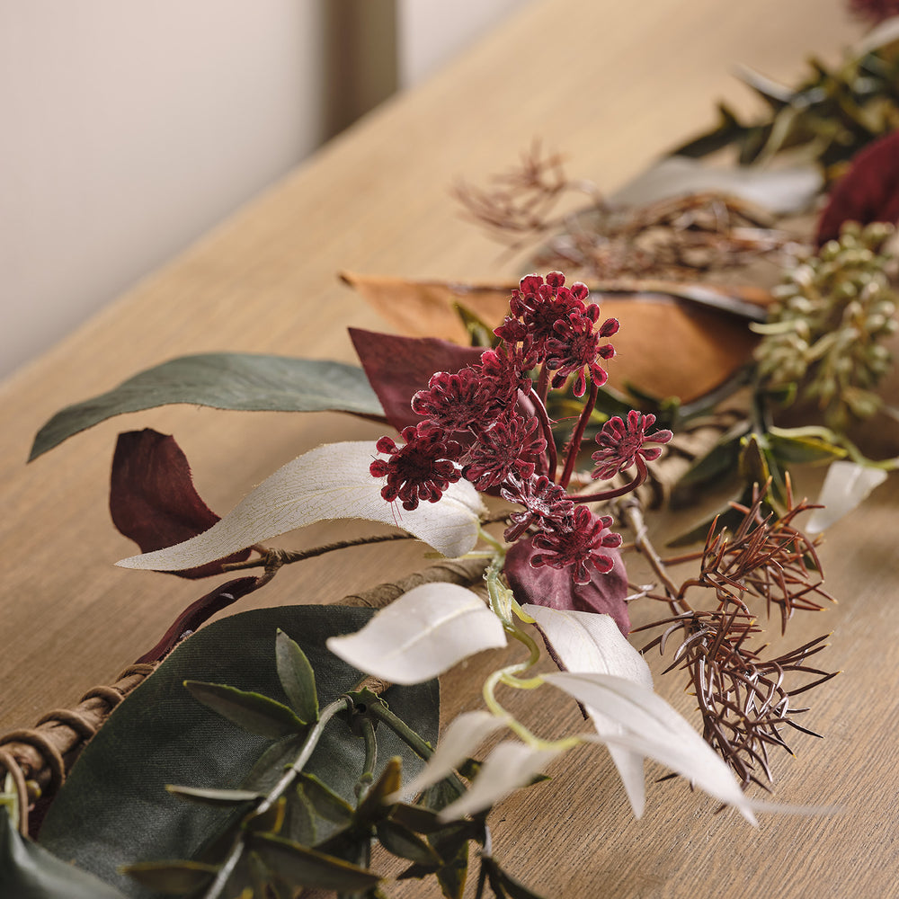 Nahaufnahme der herbstlichen Girlande mit roten Blüten und verschiedenen Blättern auf Holztisch