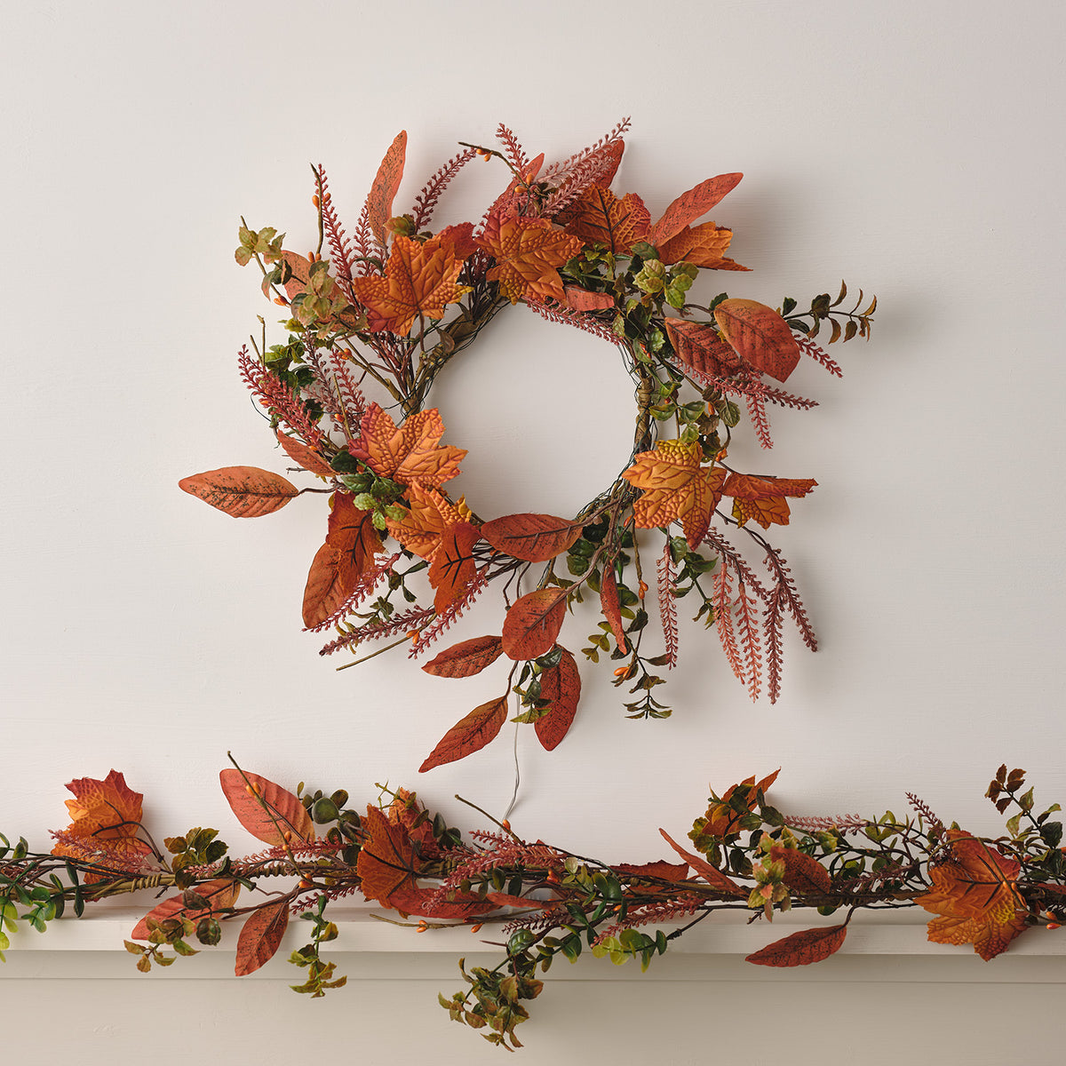 Herbstgirlande mit orangefarbenen Ahornblättern und grünen Zweigen auf weißem Regal
