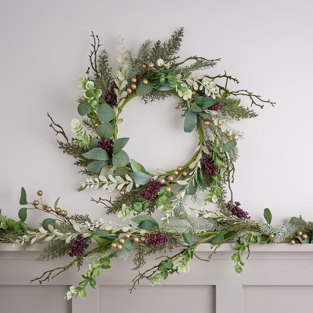 Weihnachtskranz mit goldenen Beeren und winterlichem Laub über einer passenden Girlande an einer Wand