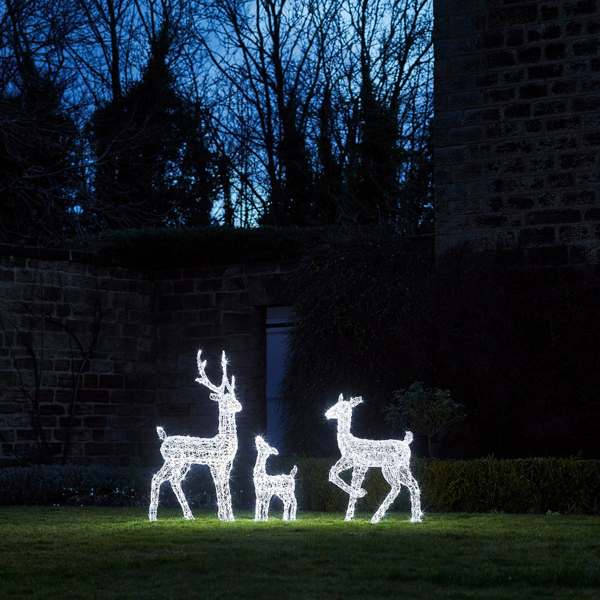 LED-Rentiere mit Weihnachtsdeko vor Holzhaus mit Laterne und Kerzen im Schnee