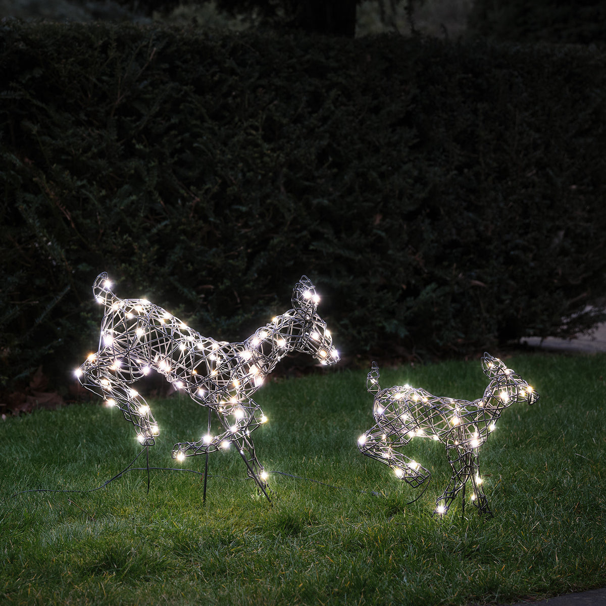 Zwei springende LED-Rentiere mit kaltweißen Lichtern auf grünem Rasen bei Dämmerung