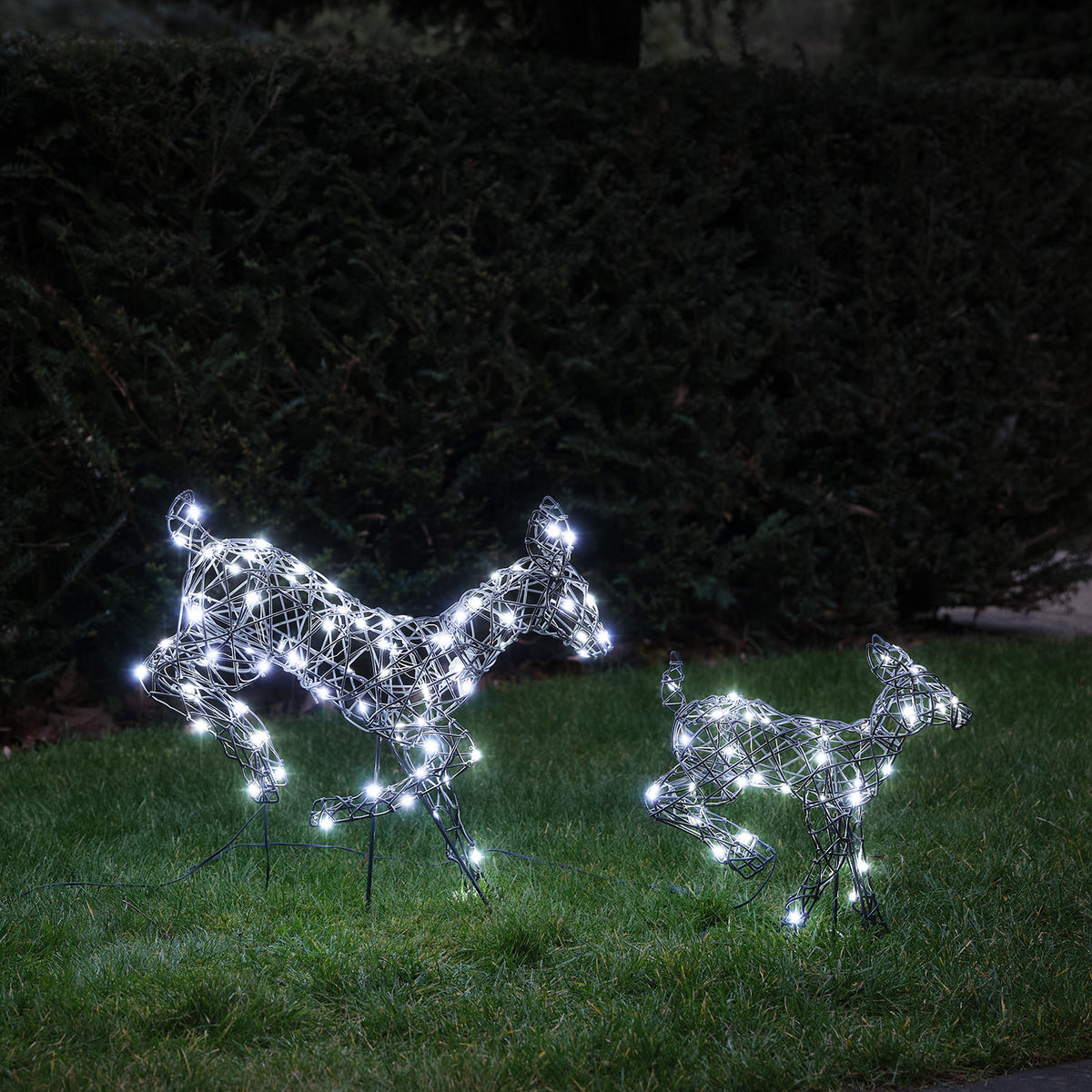 Zwei springende LED-Rentiere mit kaltweißen Lichtern auf grünem Rasen bei Nacht