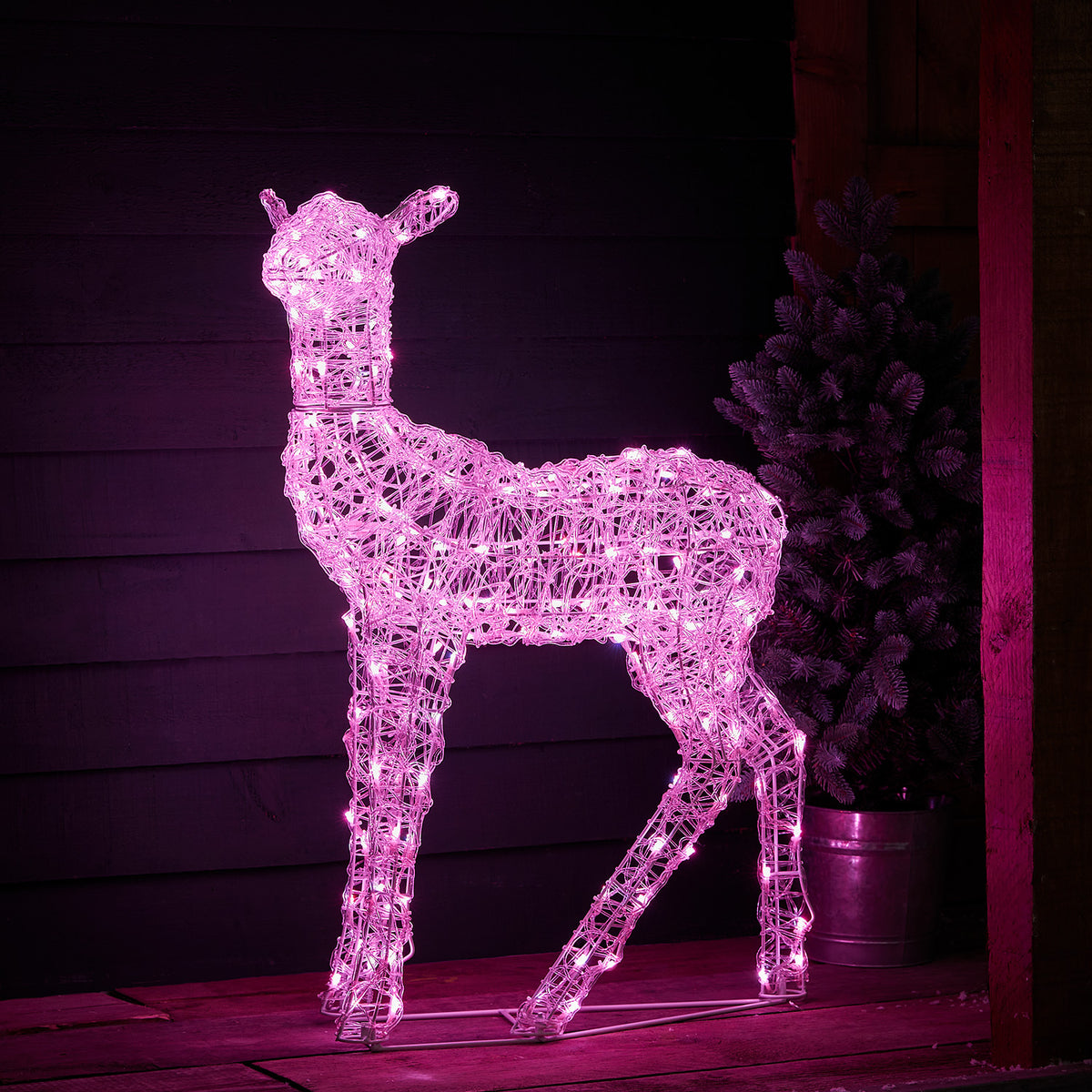 LED-Hirsch pink leuchtend vor dunkler Holzfassade auf Holzterrasse