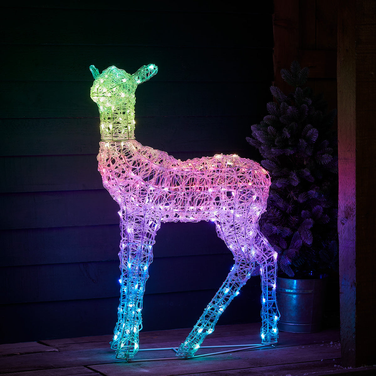 LED-Hirsch weiß leuchtend vor dunkler Holzfassade auf Holzterrasse