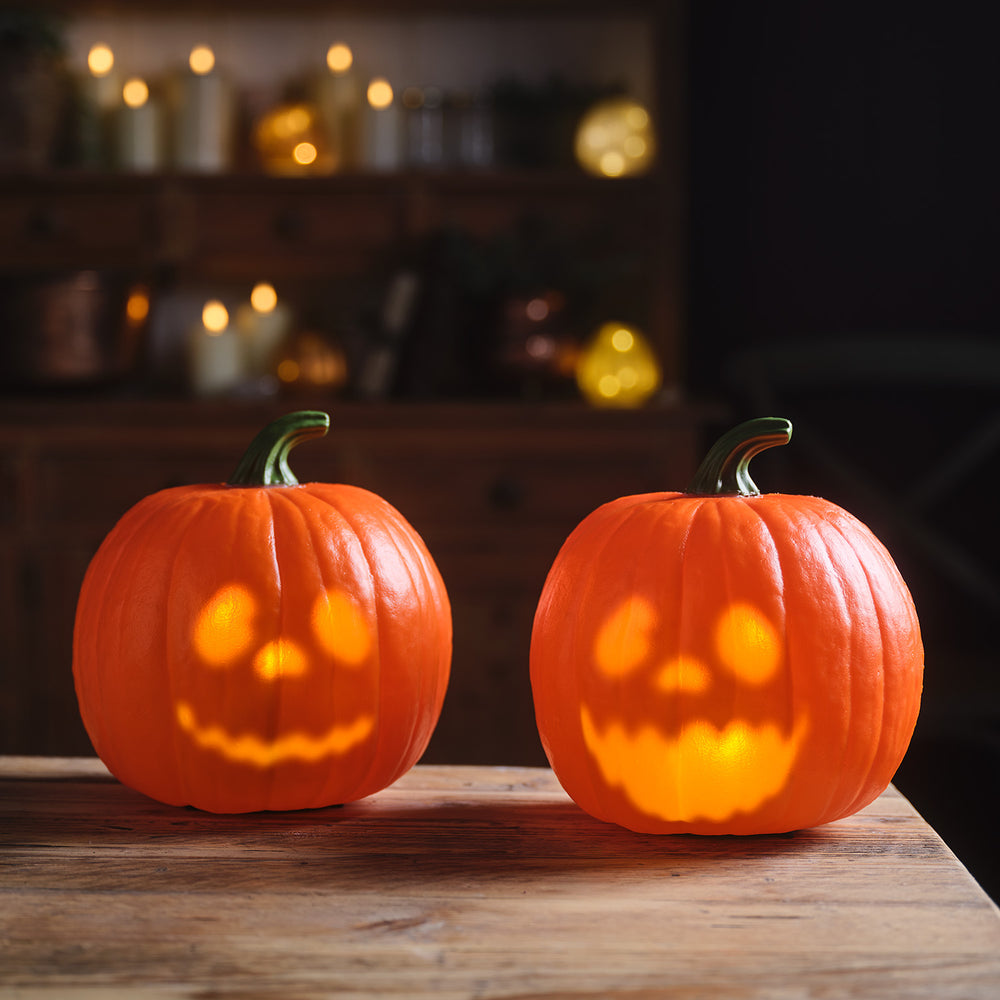 2 animierte Halloween-Kürbisse warmweiß leuchtend auf Holztisch vor dunklem Hintergrund mit Kerzen