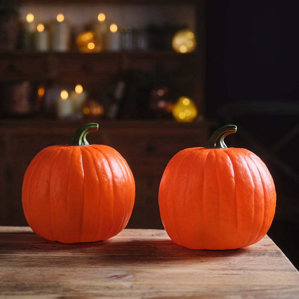 2 ausgeschaltete Halloween-Kürbisse auf Holztisch vor dunklem Hintergrund mit Kerzen