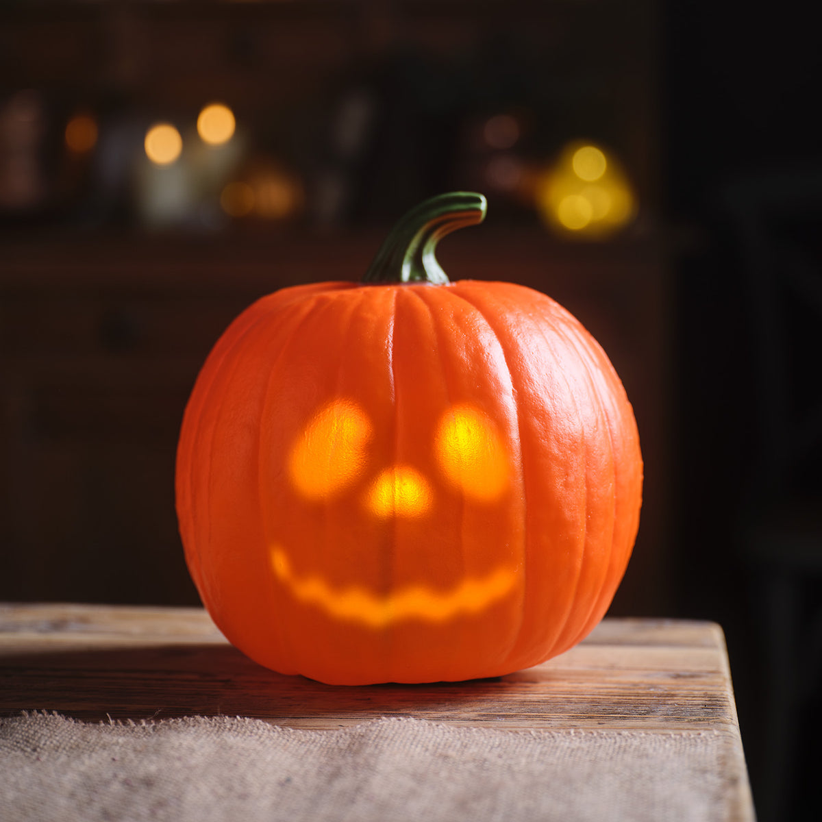 Nahaufnahme animierter Halloween-Kürbis warmweiß leuchtend auf Holztisch vor dunklem Hintergrund