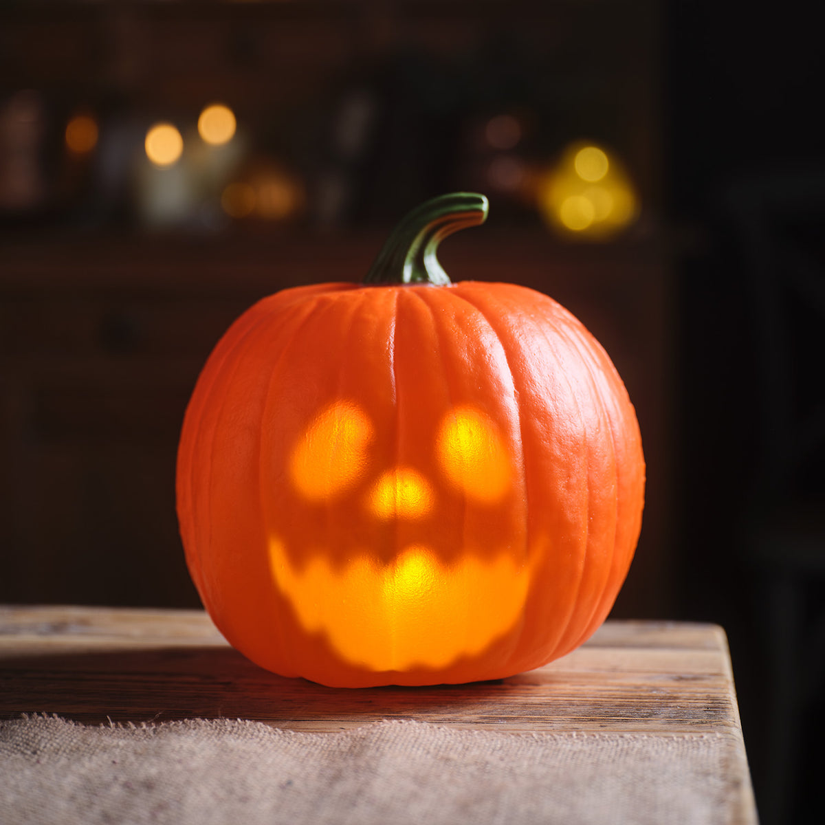 Nahaufnahme animierter Halloween-Kürbis warmweiß leuchtend auf Holztisch mit Stoffdecke