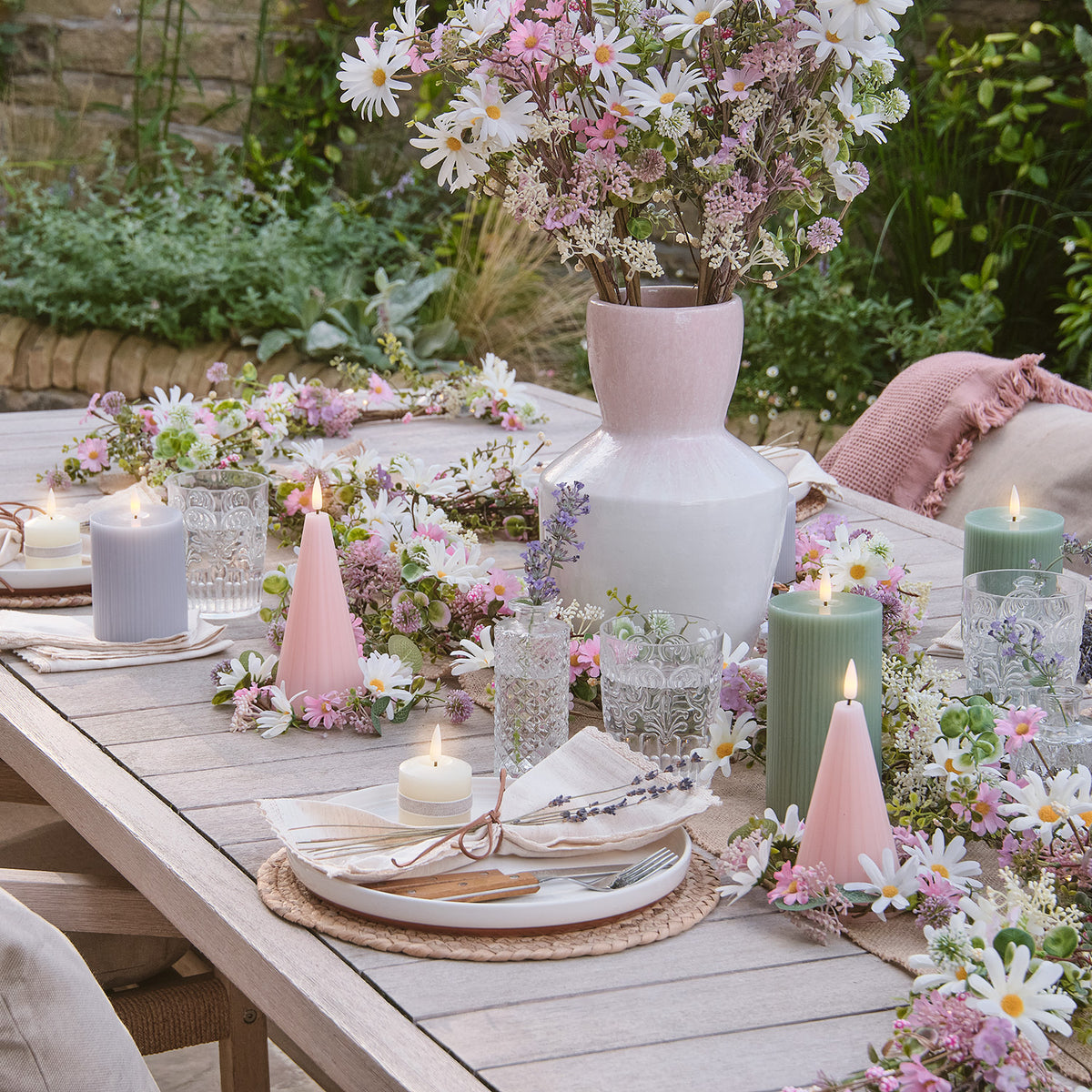Tischdekoration mit rosa-weißer Keramikvase, Kerzen und künstlichen Gänseblümchen im Garten