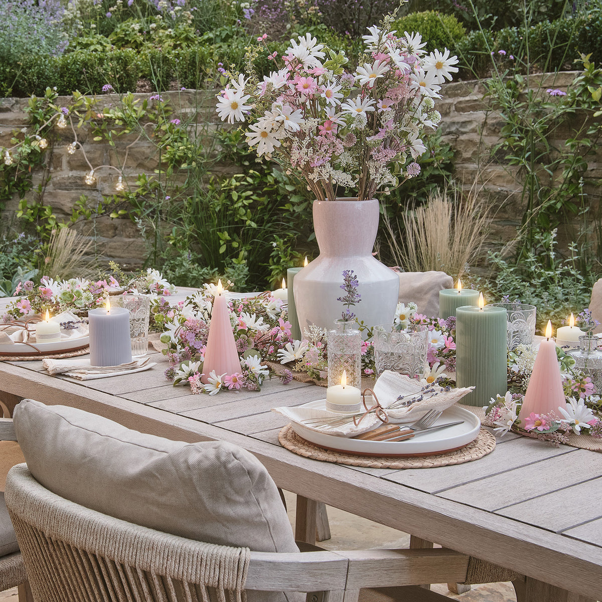 Gedeckter Gartentisch mit rosa-weißer Keramikvase, Kerzen und künstlichen Blumenarrangements