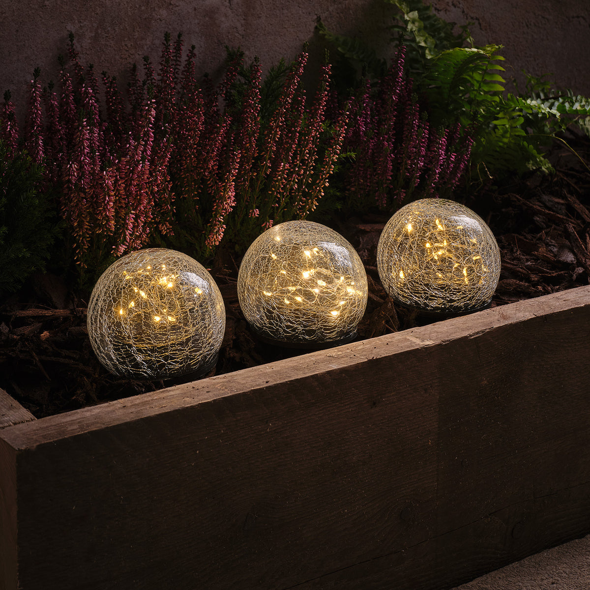 Drei leuchtende Solar-Gartenstecker mit warmweißen LEDs in Crackle-Glaskugeln im Beet