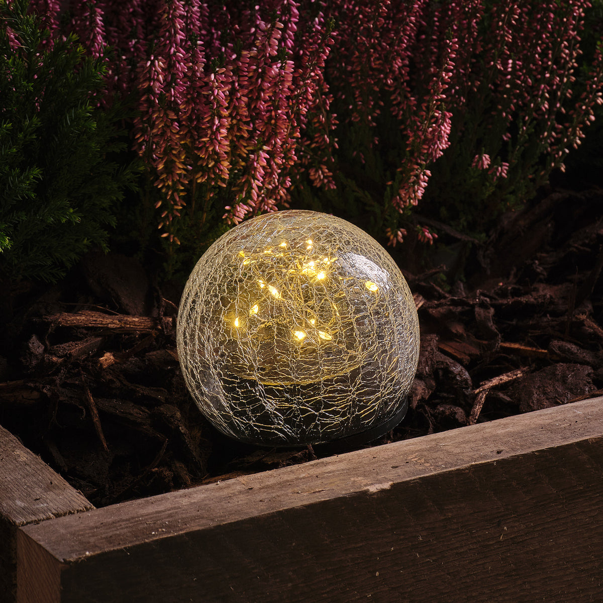 Nahaufnahme einer leuchtenden Crackle-Glaskugel mit warmweißen LEDs im Gartenbeet