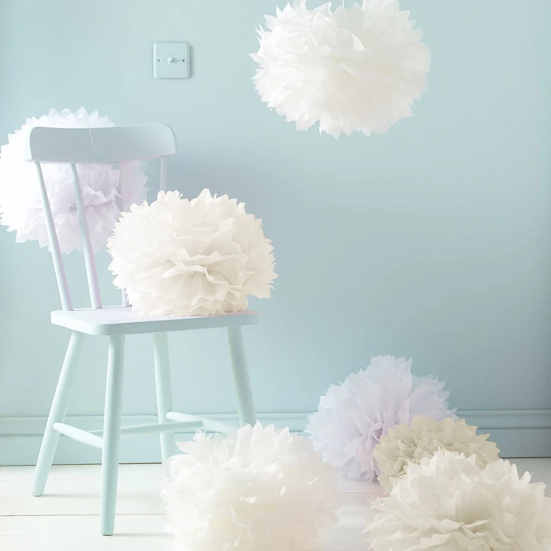 Neun Papierpompons in Weiß, Rosa und Crème dekorativ um einen weißen Stuhl arrangiert
