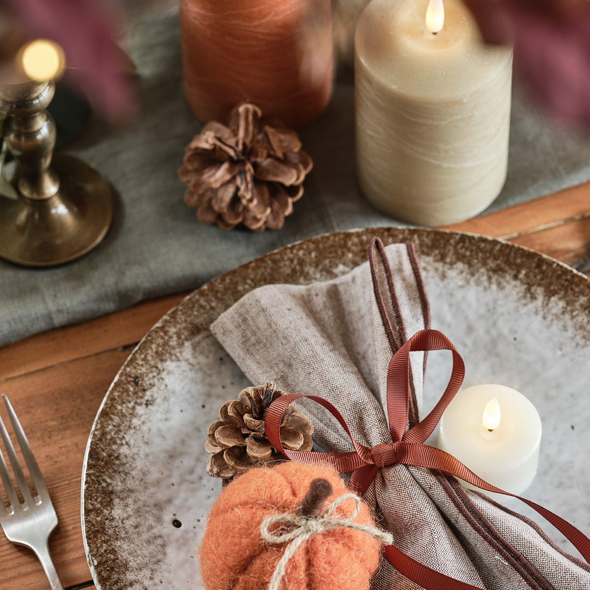 Herbstliche Tischdeko mit Filz-Kürbis, Zapfen, Kerzen und Stoffserviette auf Teller