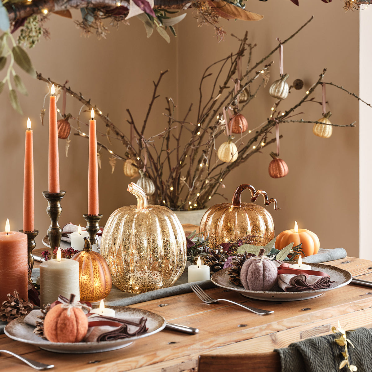 Herbstlich gedeckter Holztisch mit Kerzen, Glas-Kürbissen und Filz-Kürbissen als Dekoration