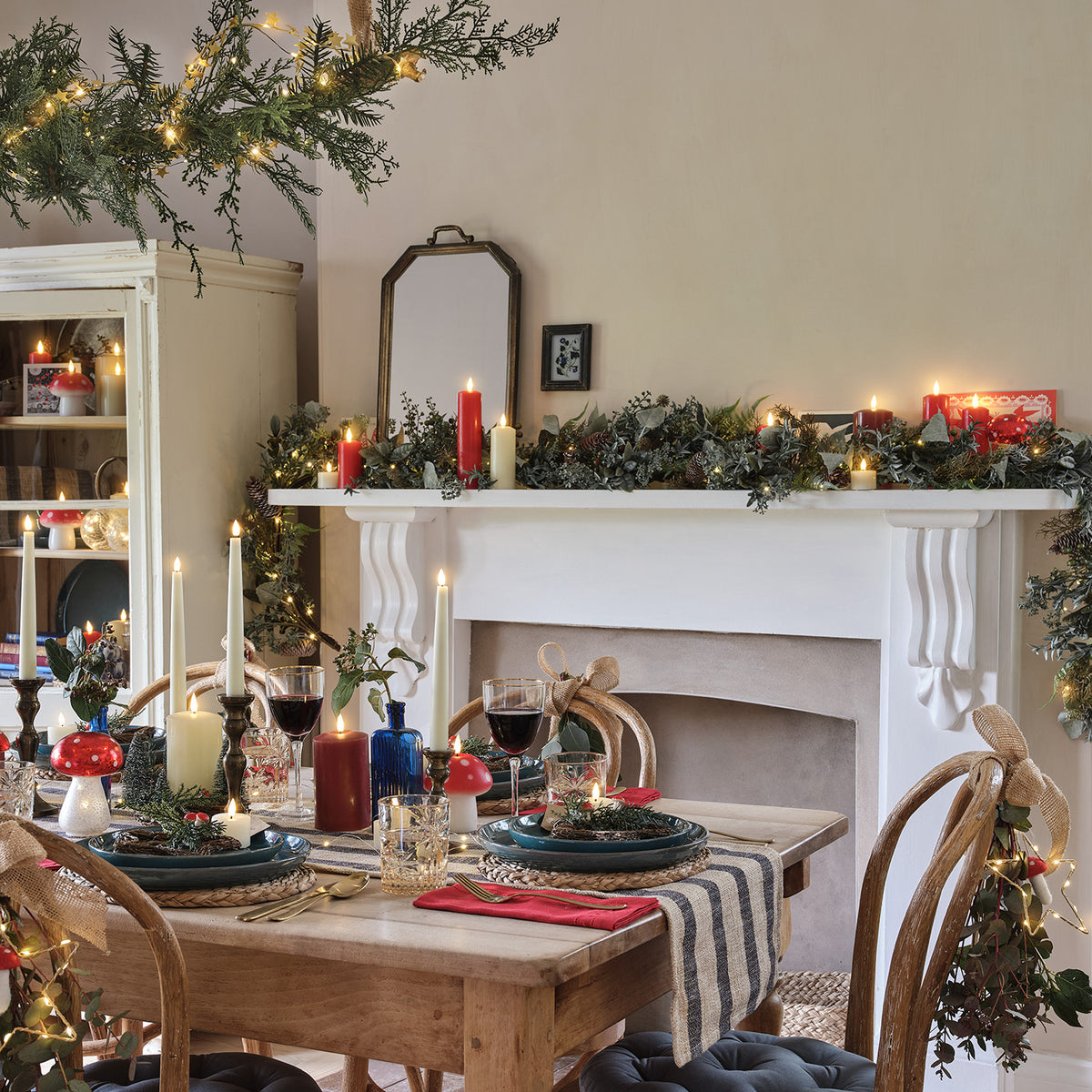 Weihnachtlich gedeckter Tisch mit Kerzen, Pilzen und Tannenkranz vor Kamin