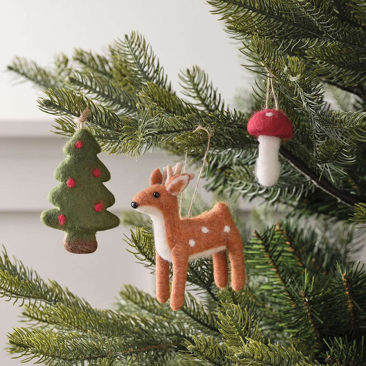 Filzanhänger Rentier, Tannenbaum und Pilz hängen an Zweigen eines Weihnachtsbaums