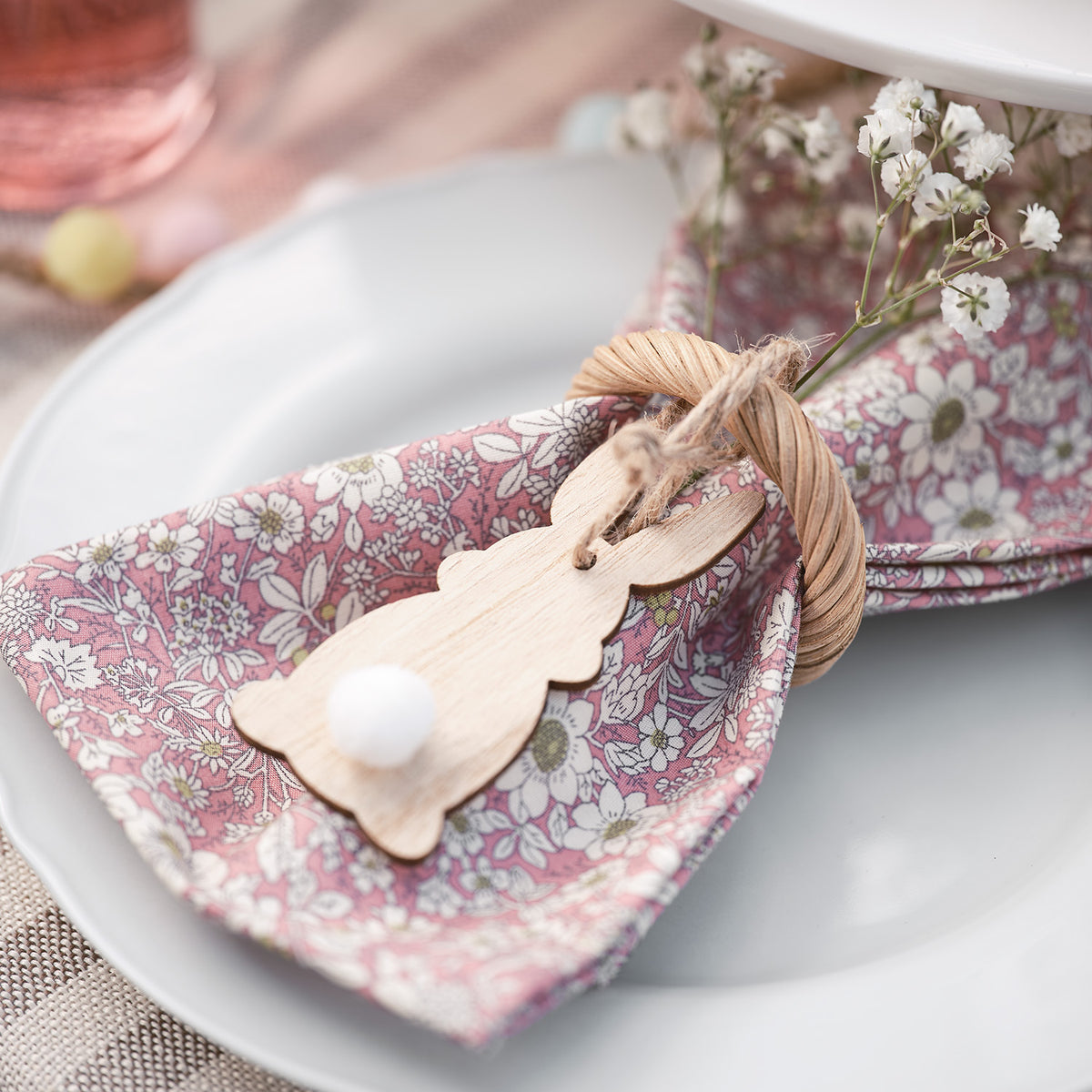 Holzhasenanhänger mit Pomponschwanz als Serviettenring auf rosa gemusterter Stoffserviette
