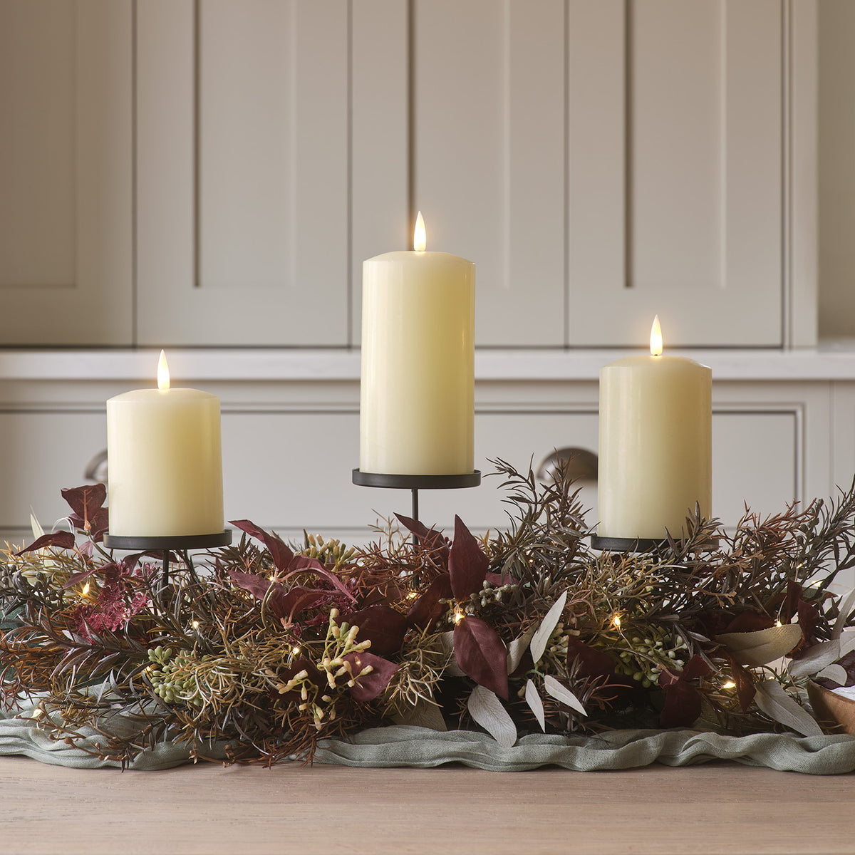 Kerzenhalter mit drei brennenden elfenbeinfarbenen LED Stumpenkerzen und herbstlichem Kunstlaub dekoriert