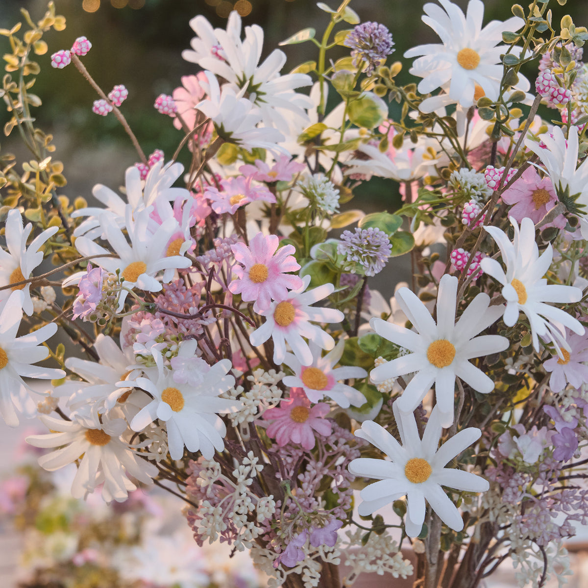 Detailaufnahme künstlicher Frühlingsstrauß mit weißen Gänseblümchen und rosa Blüten bei Sonnenlicht