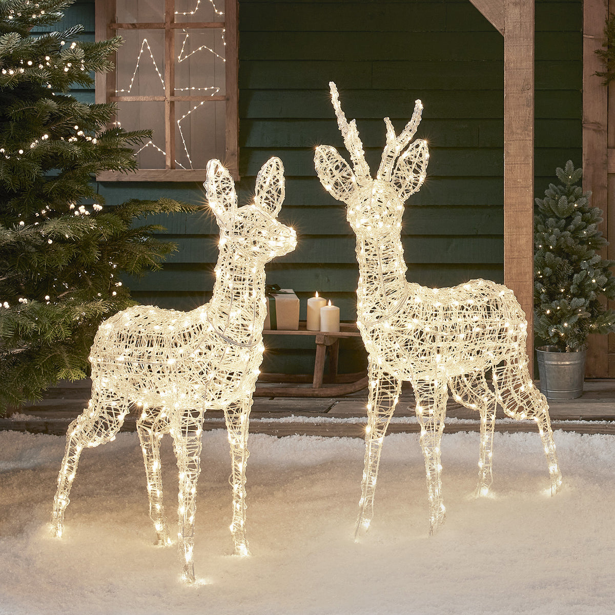 Zwei bicolore LED-Rentiere in warmweiß leuchtend vor Hauswand mit Weihnachtsdeko