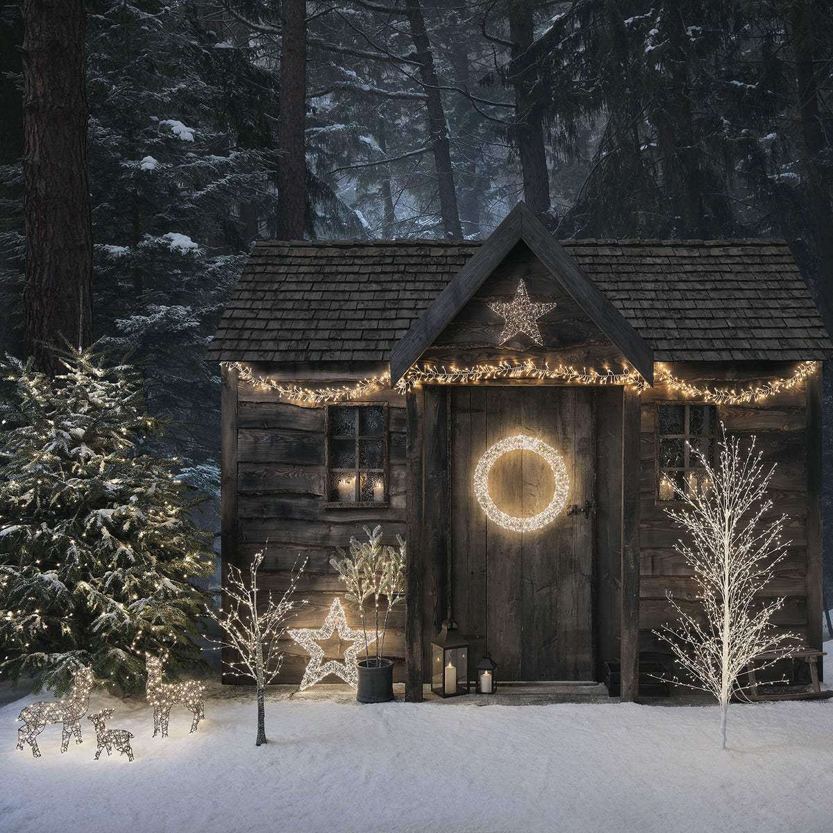 Winterliche Gartenhütte mit LED-Lichterdekoration und beleuchteter Mini LED-Rentierfamilie im Schnee