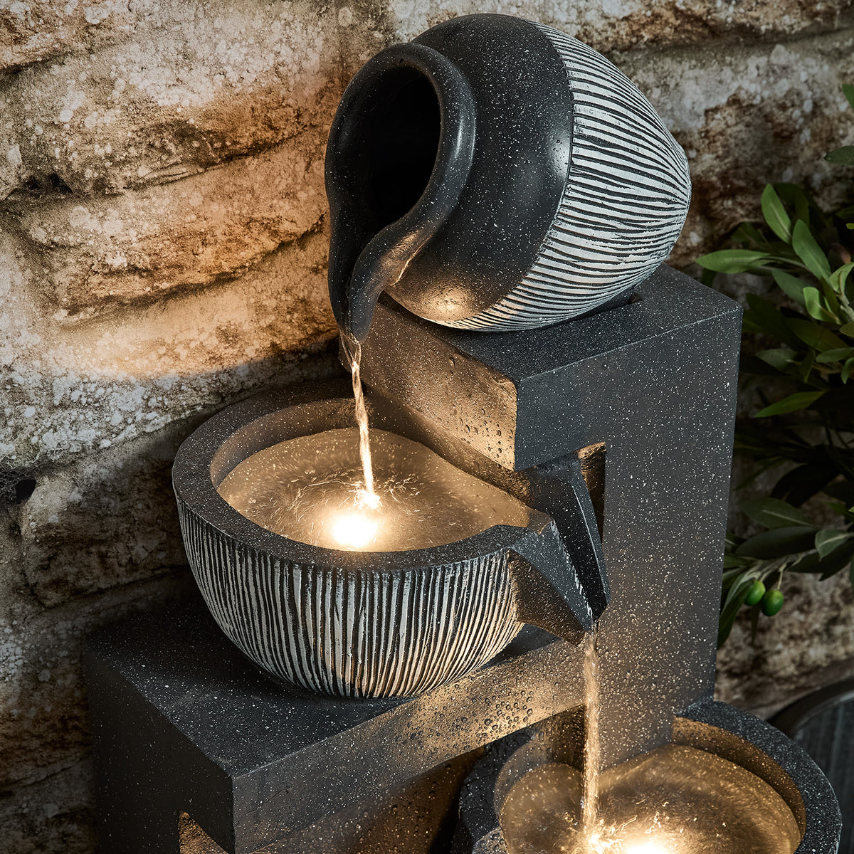 Nahaufnahme des oberen Bereichs des Gartenbrunnens mit fließendem Wasser und warmweißer LED-Beleuchtung