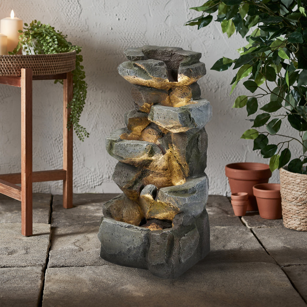 Grau strukturierter Gartenbrunnen in Felsenoptik mit warmweißen LEDs, dekorativ im Raum platziert