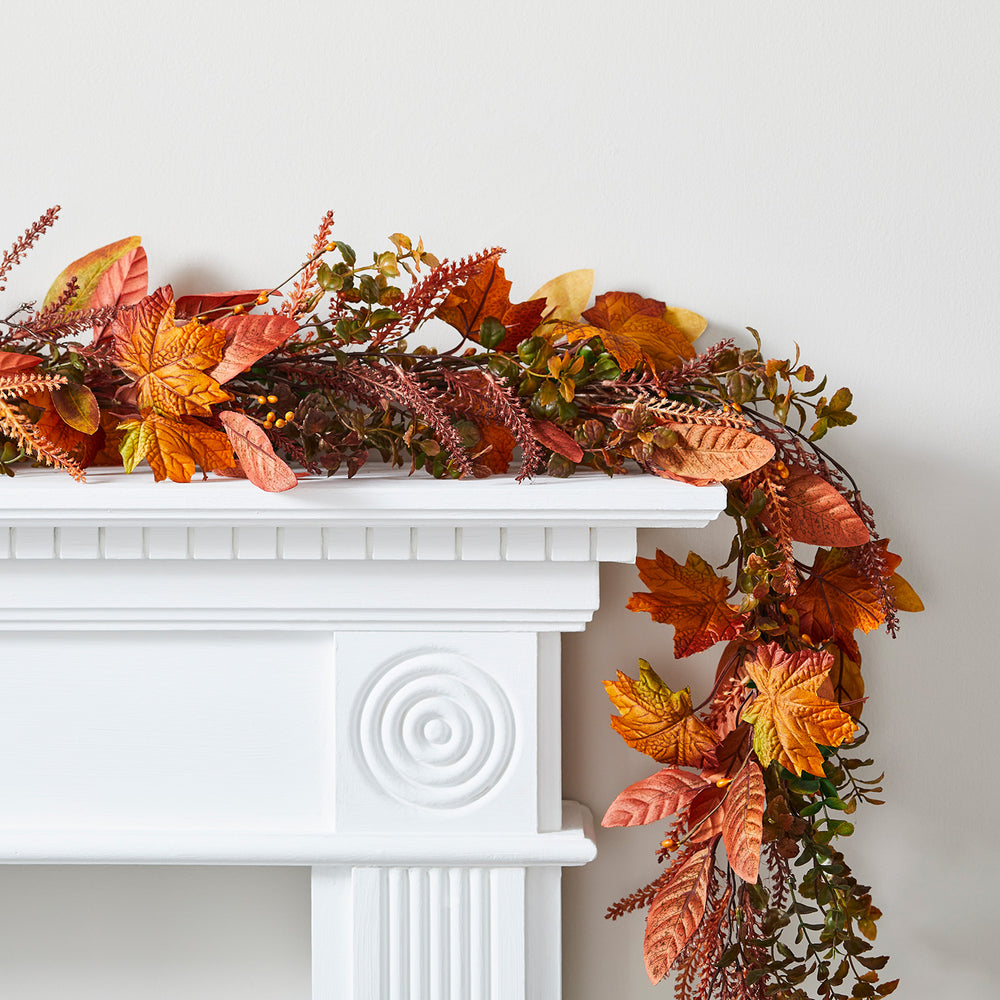 Herbstgirlande mit orangefarbenen Ahornblättern und Beeren auf weißem Kaminsims