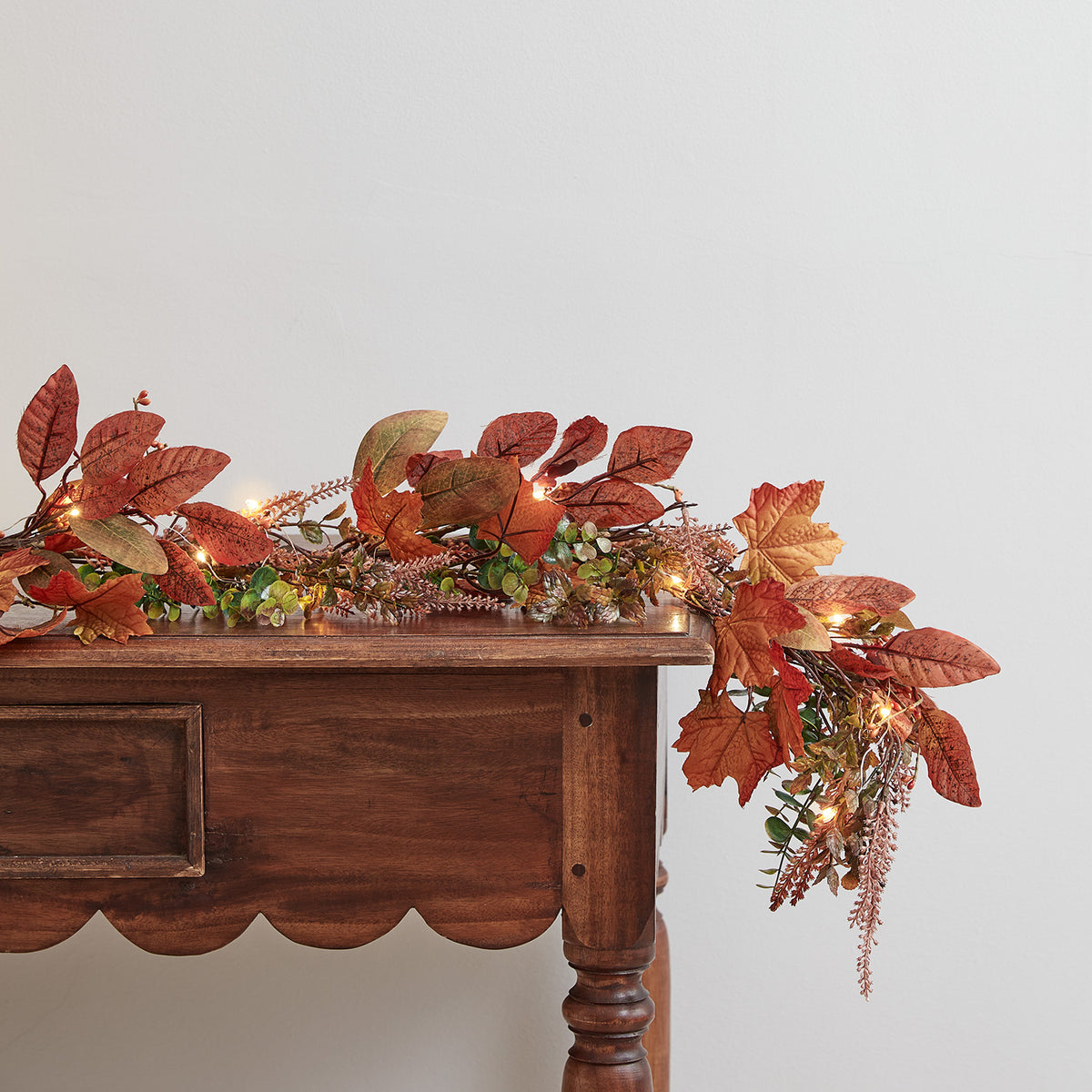 Herbstliche Girlande mit beleuchteten Ahornblättern auf braunem Holztisch