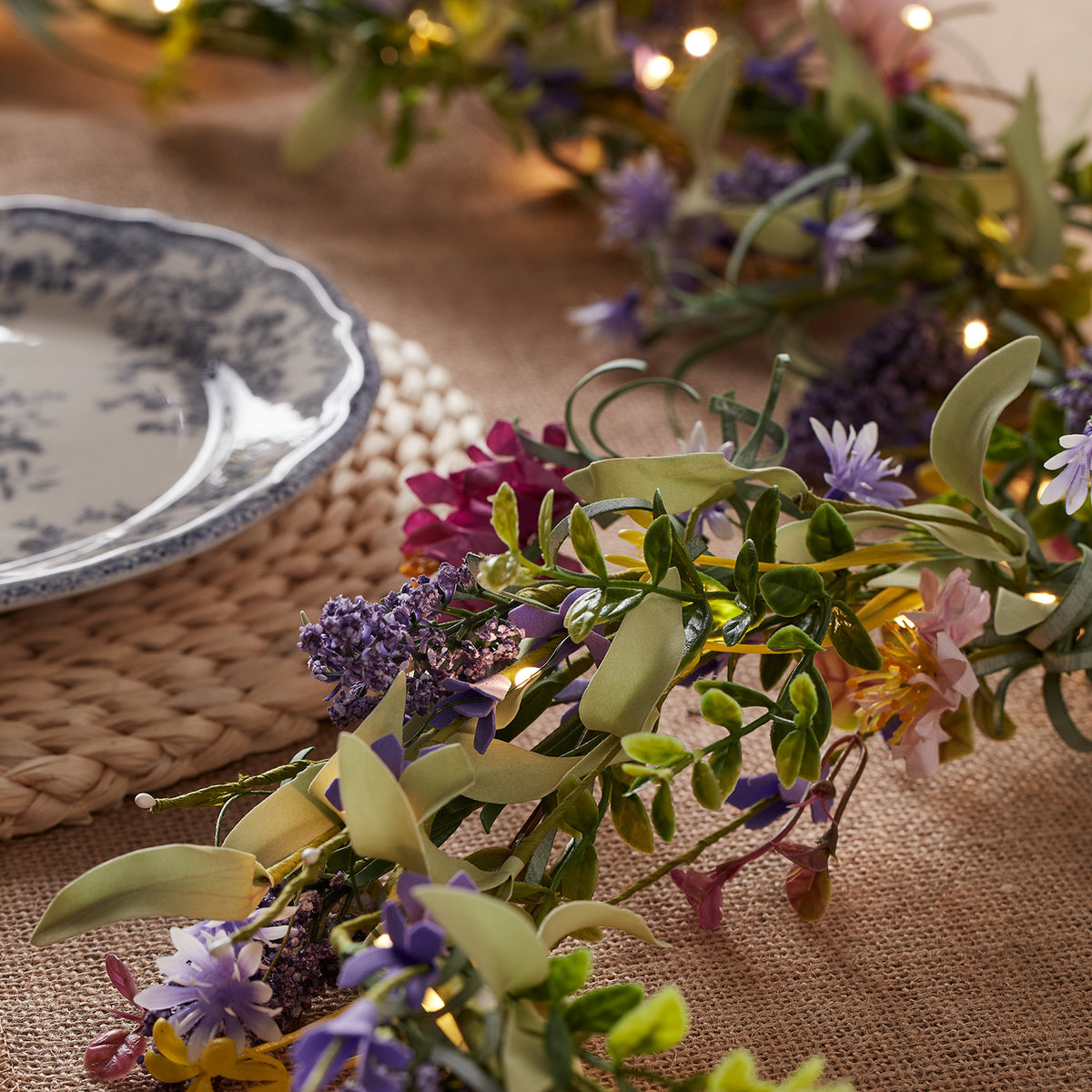 Nahaufnahme der beleuchteten Lavendel- und Blumenfrühlingsgirlande auf Tisch mit blau-weißem Teller