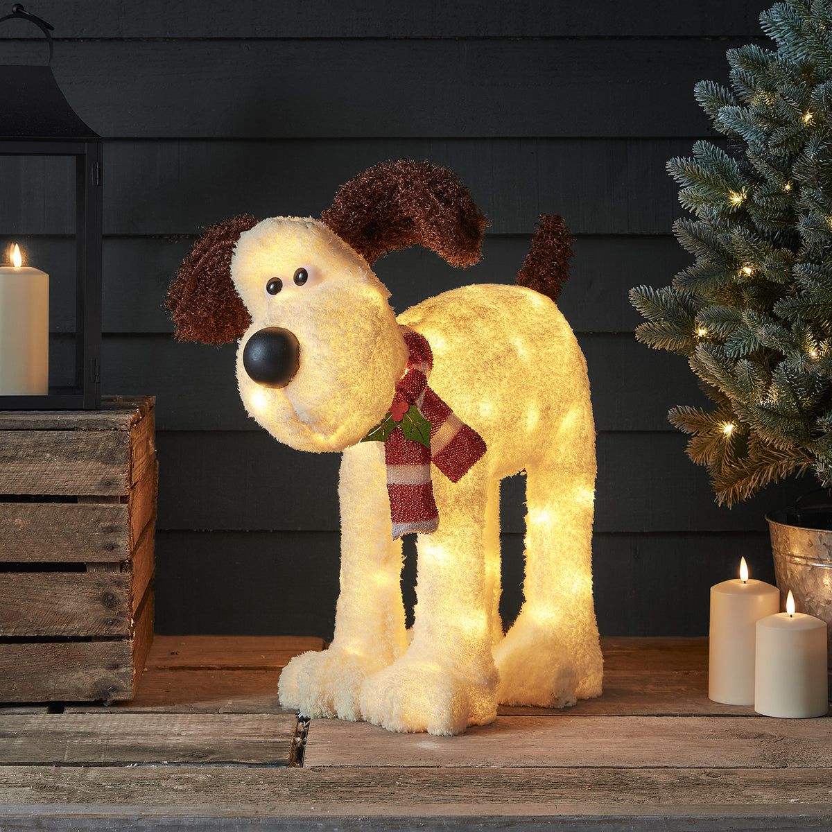Beleuchtete Gromit LED-Figur mit rot-weißem Schal neben Kerzen und Tannenzweig