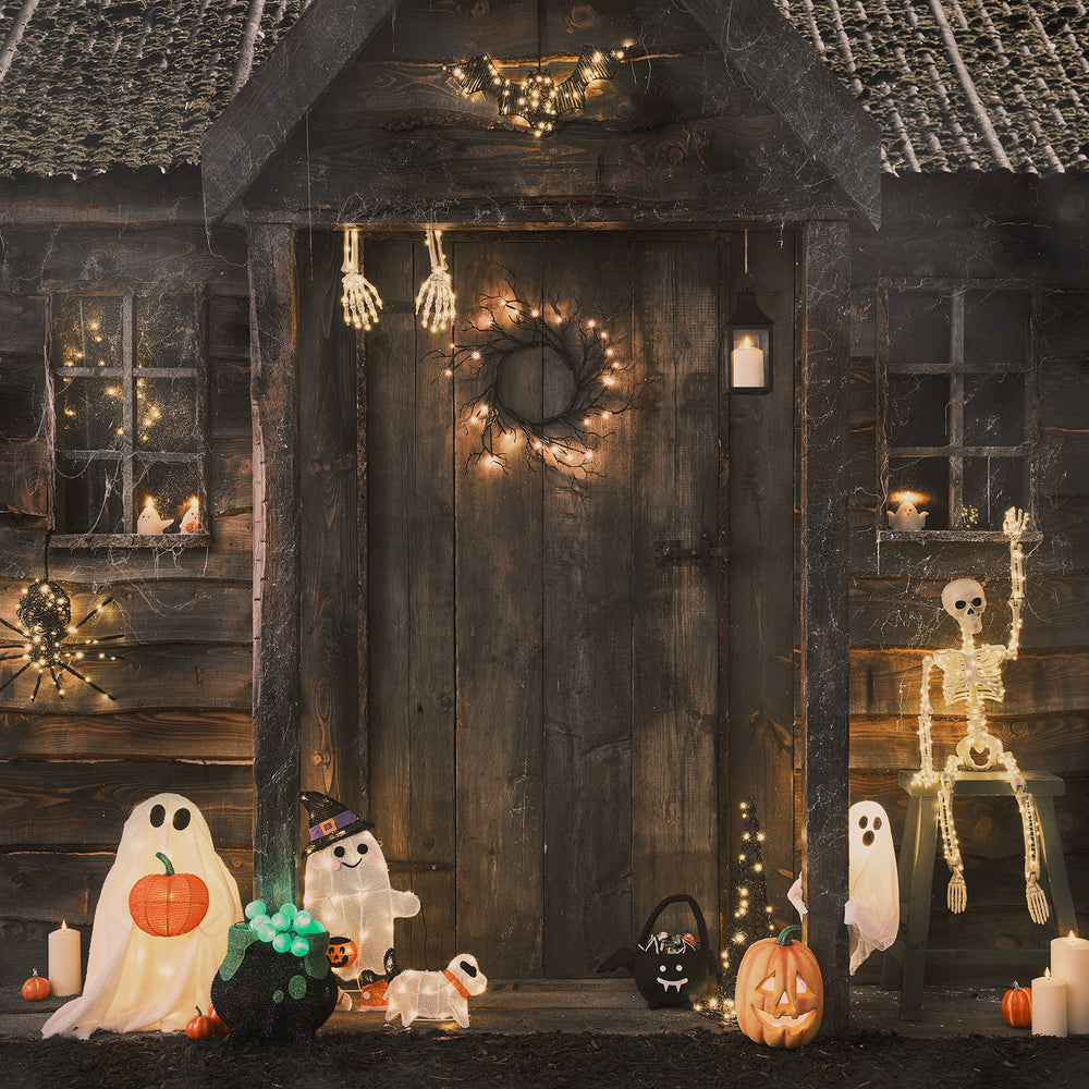 Halloween-Deko vor Holztür mit Skelett-Armen, Kürbissen und Geisterlichtern