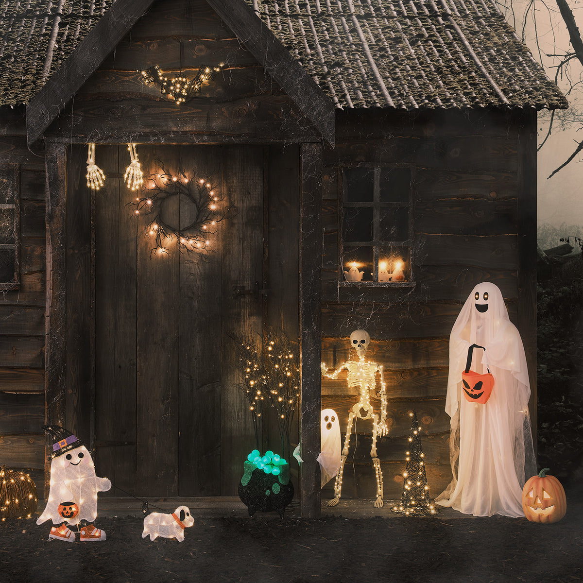 LED-Geist mit orangefarbener Tasche warmweiß leuchtend neben Skelett und Halloween-Deko vor Holzhütte