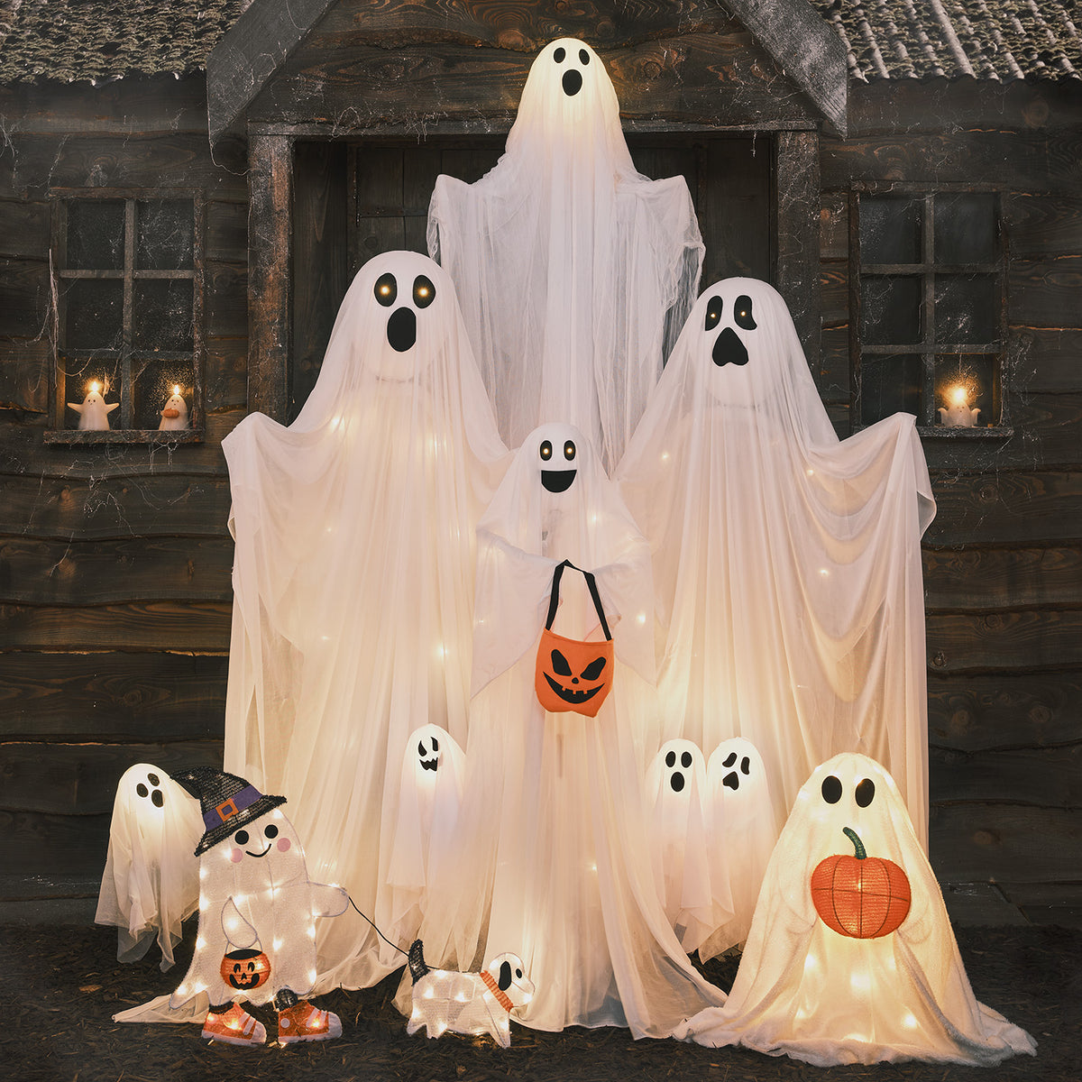 LED-Geisterfamilie warmweiß leuchtend mit weiteren Halloween-Figuren vor Holzhütte