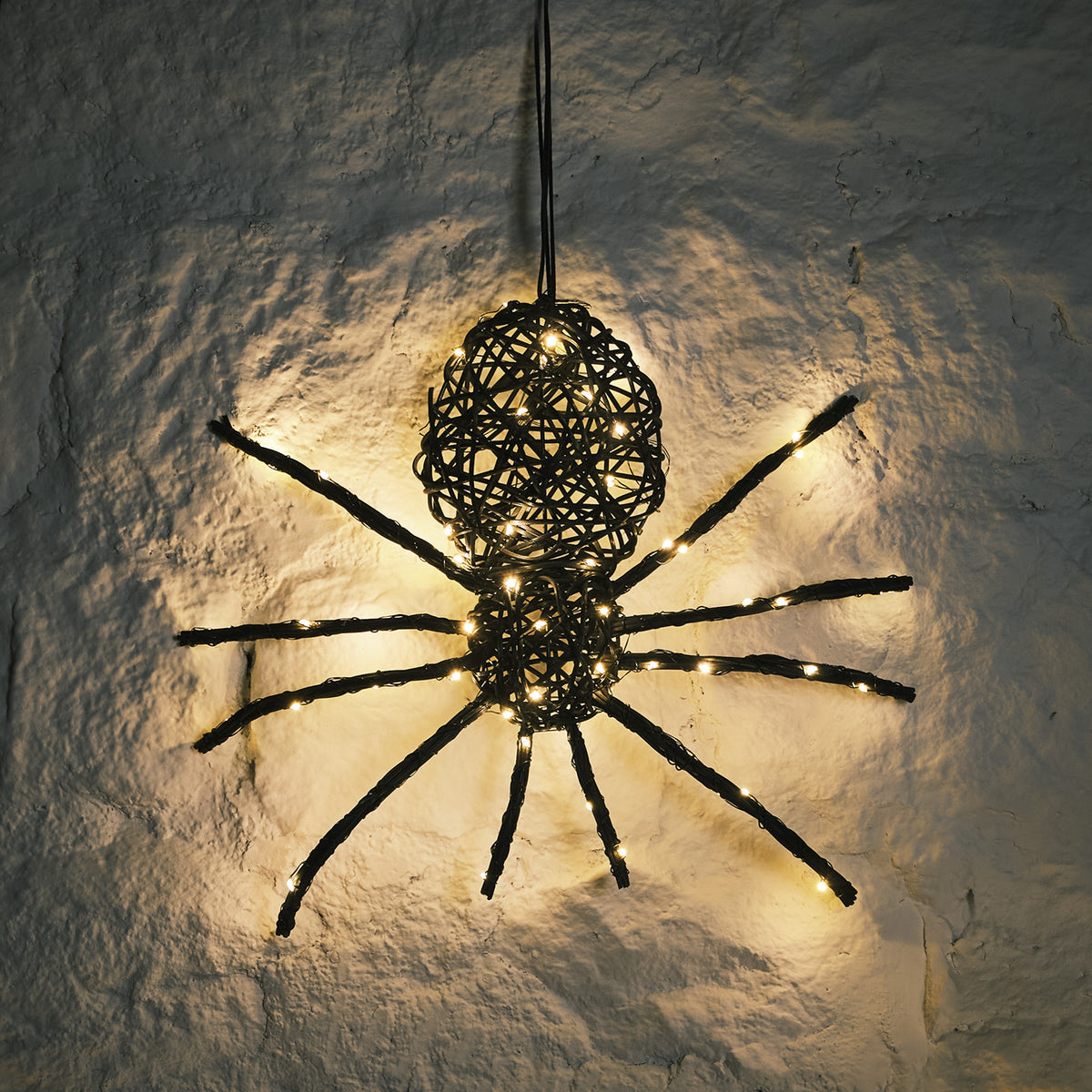 Beleuchtete Rattan Spinne mit warmweißen LEDs an weißer Wand im Dunkeln