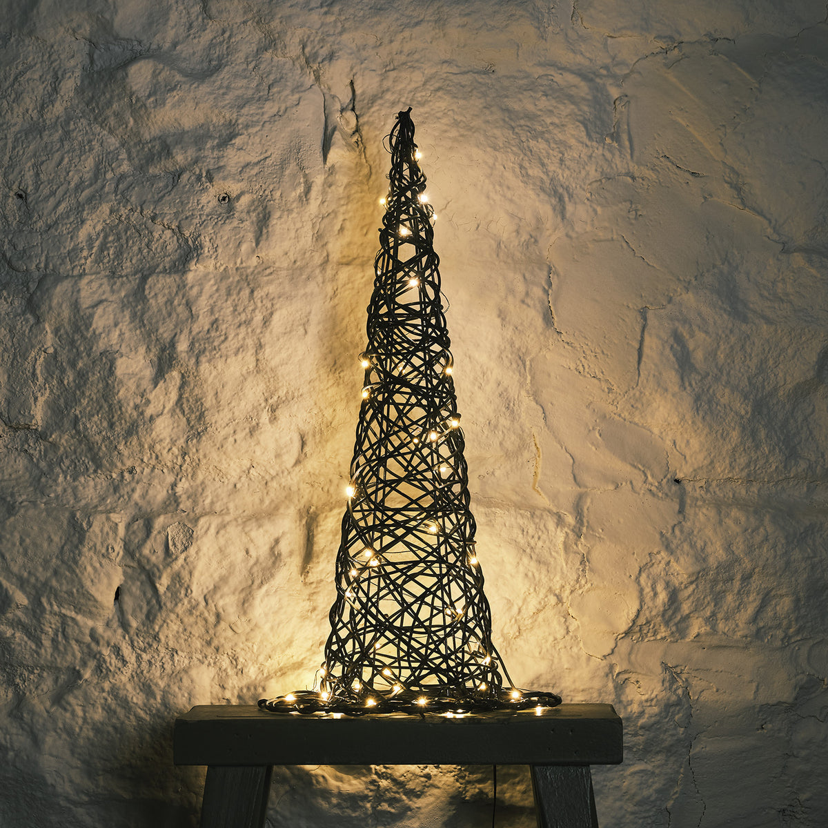 Rattan Hexenhut mit warmweißen LEDs auf grauem Hocker vor weißer Steinwand, von oben fotografiert