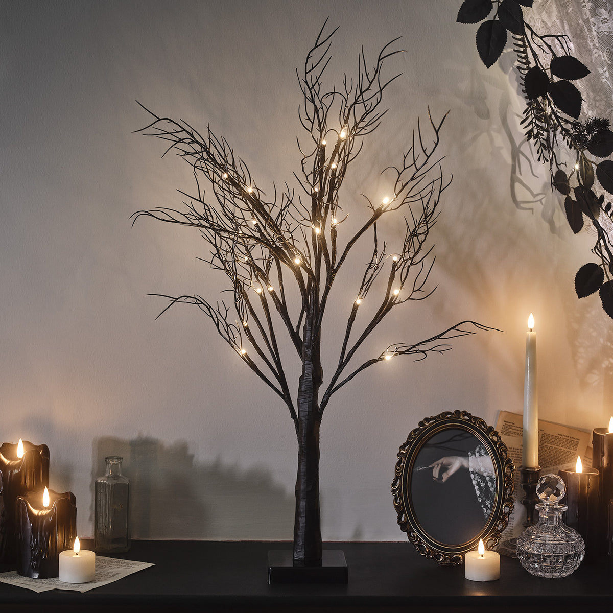 Schwarzer Halloween-Dekobaum mit leuchtenden Micro LEDs auf einem Tisch neben Kerzen und Spiegel