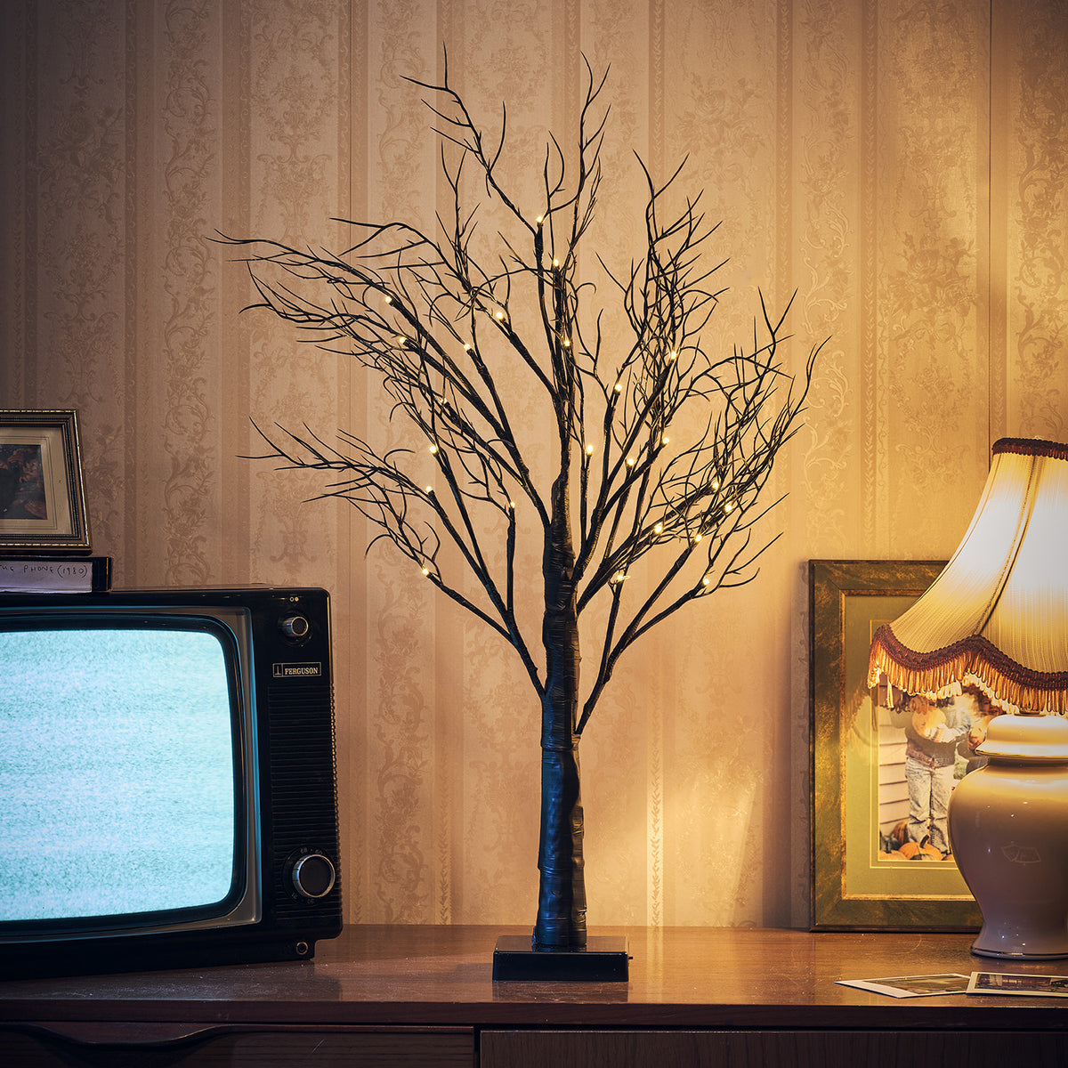 Beleuchteter schwarzer Halloween-Dekobaum auf Kommode neben Fernseher und Lampe