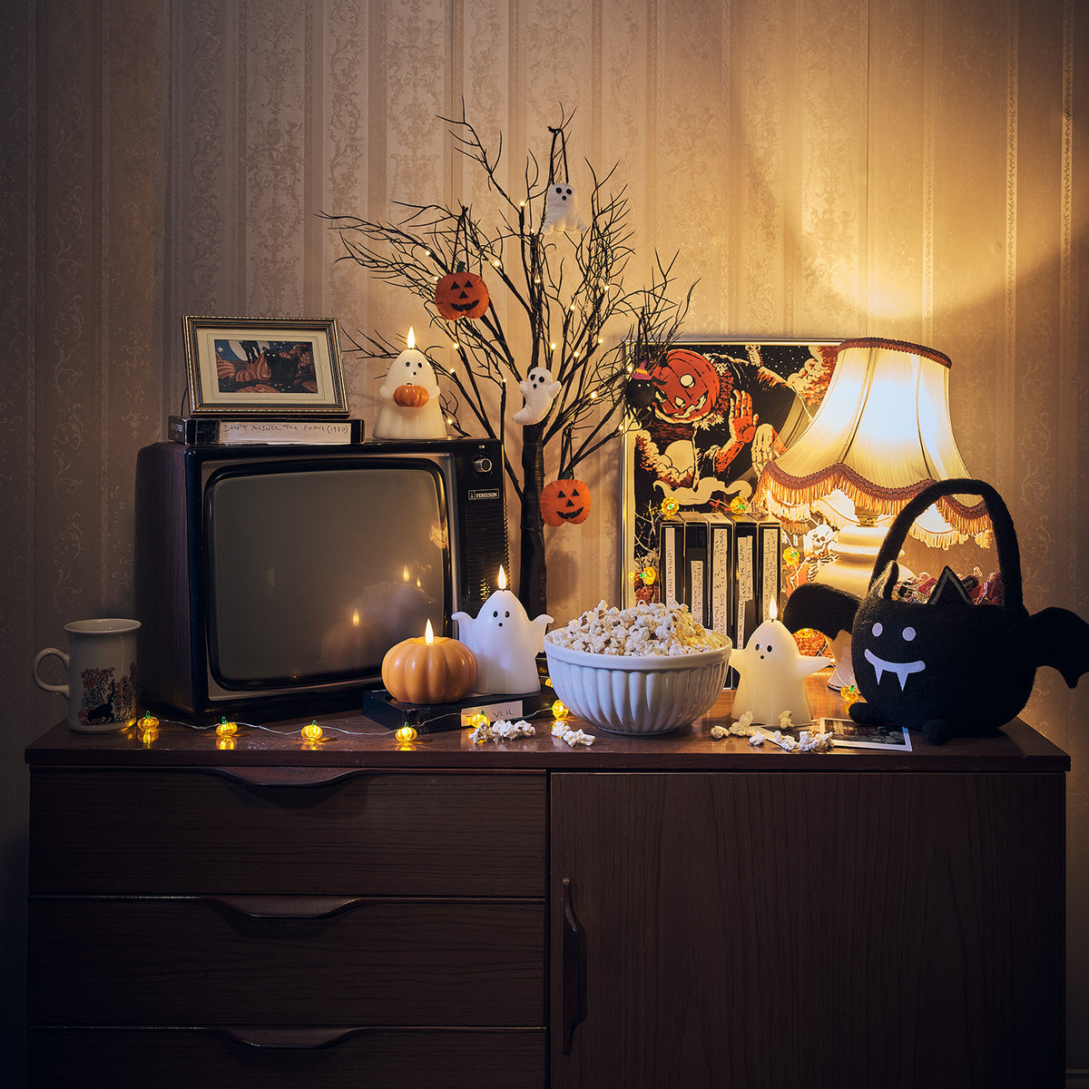 Halloween-Dekobaum mit Mini-Kürbissen und Geisteranhängern auf Kommode mit Popcorn und Deko