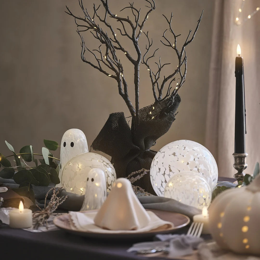 Halloween-Tischdeko mit LED-Geistern aus Konfettiglas, Kerzen und Zweigen