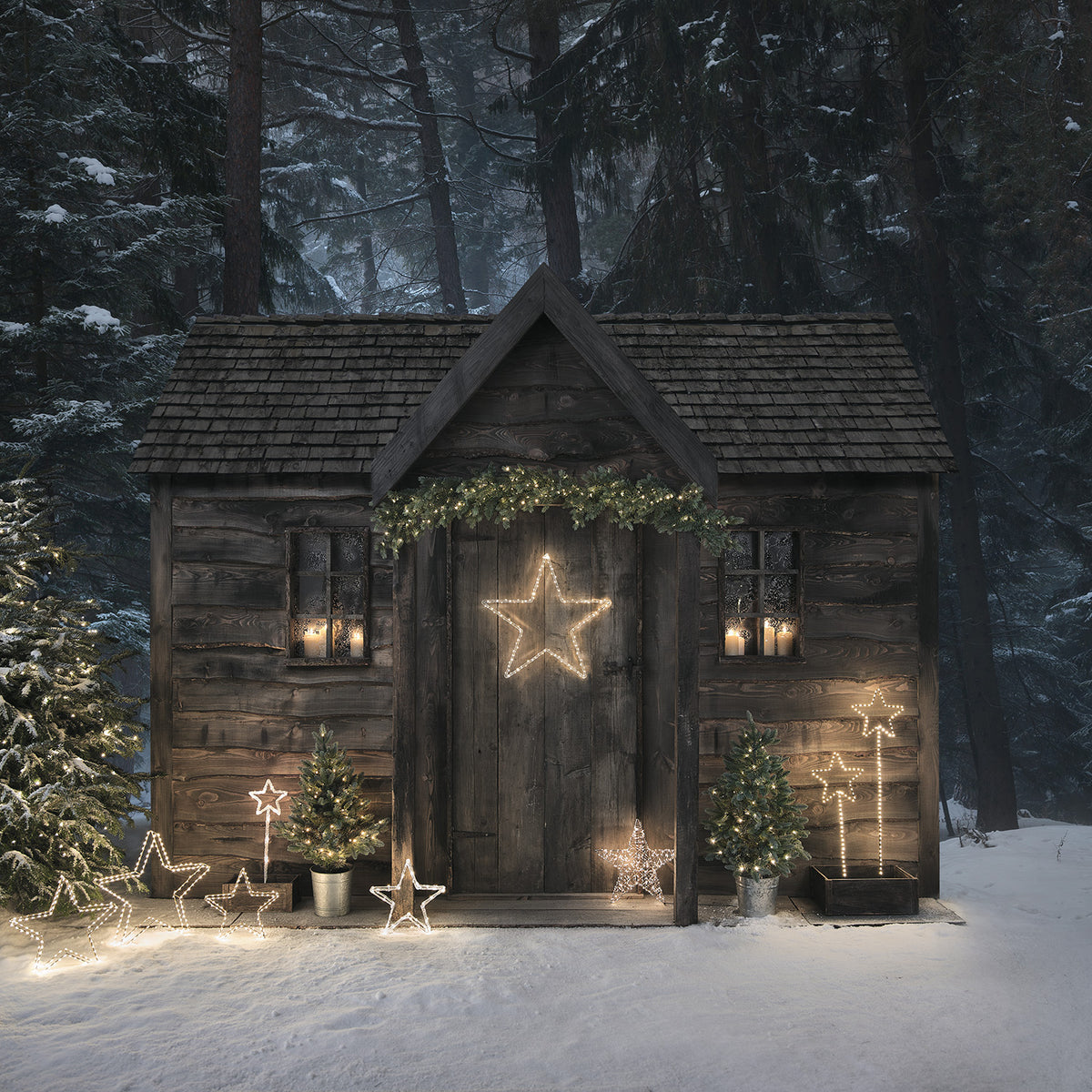 Verschneite Hütte mit mehreren leuchtenden Sternen und Tannenbäumen im Winter