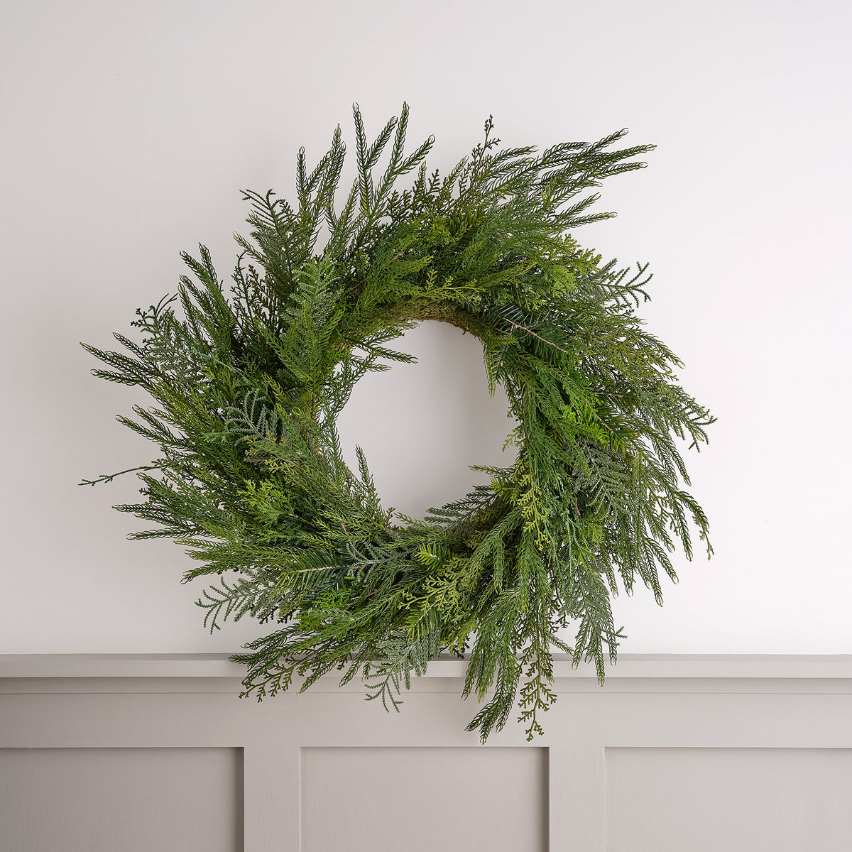 60 cm großer Weihnachtskranz aus künstlichem Zypressen-Nadelwerk an weißer Wand