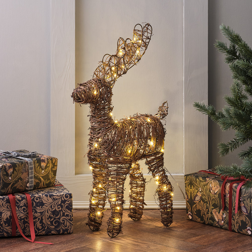 Mini LED Rentier aus braunem Rattan mit warmweißen Lichtern neben Weihnachtsgeschenken