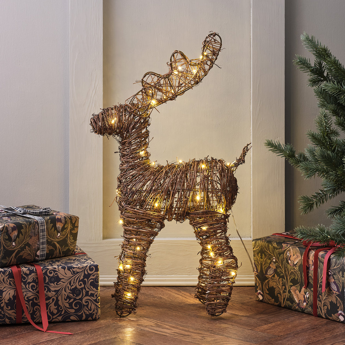 Seitenansicht des beleuchteten Rattan Rentiers mit Weihnachtsgeschenken und Tannenzweig